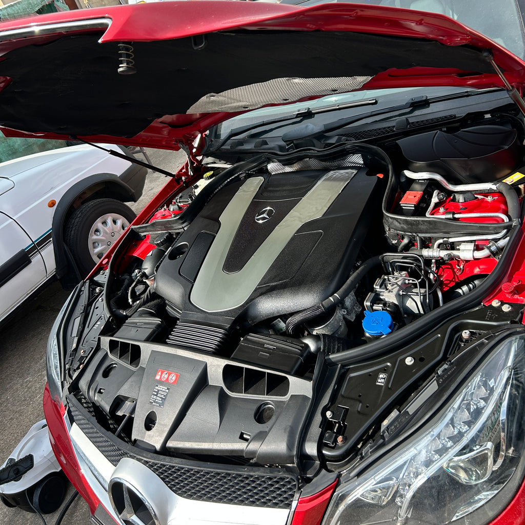 Close-up of a car engine bay with visible branding in an urban setting.