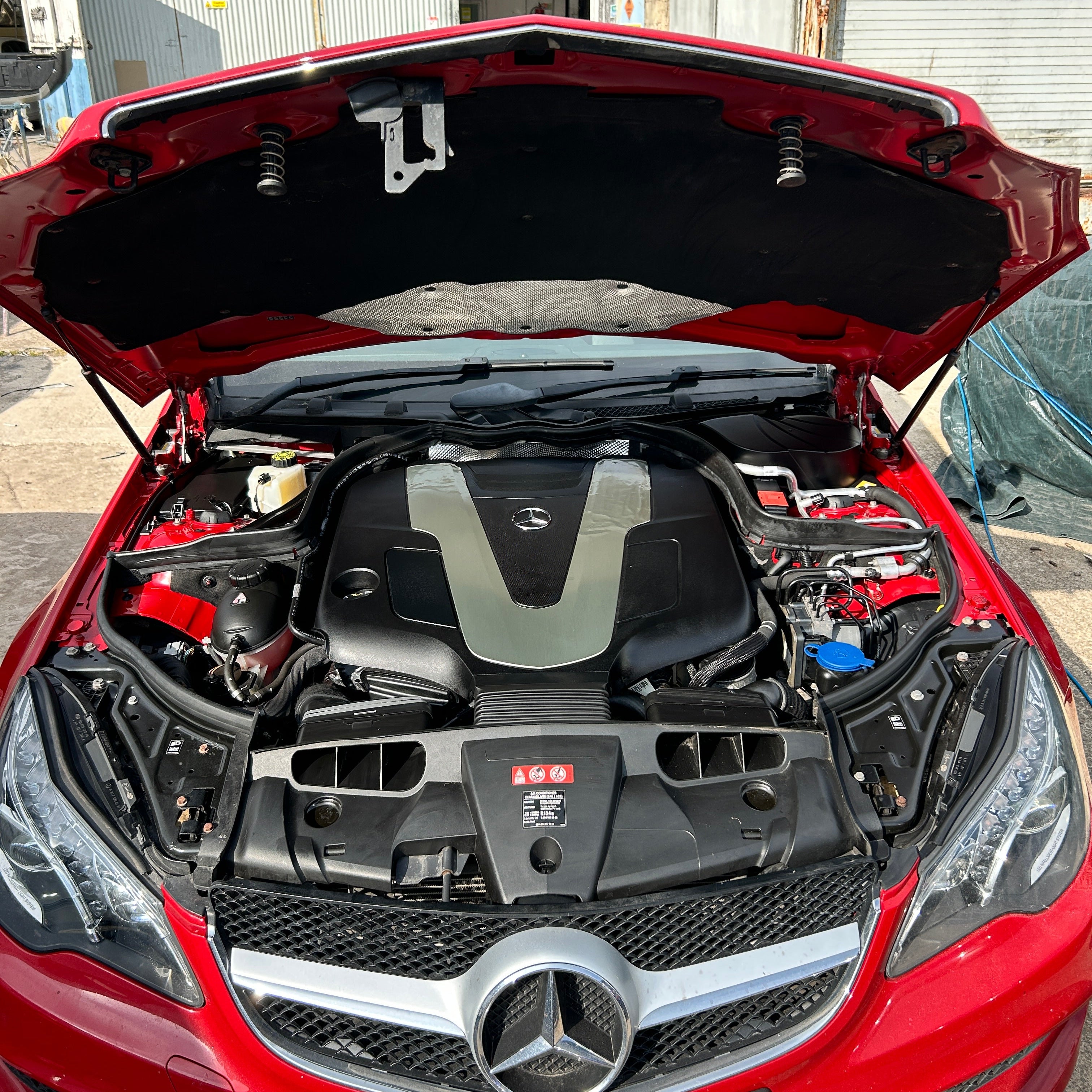 Red car with open hood showing engine compartment, brand logo visible