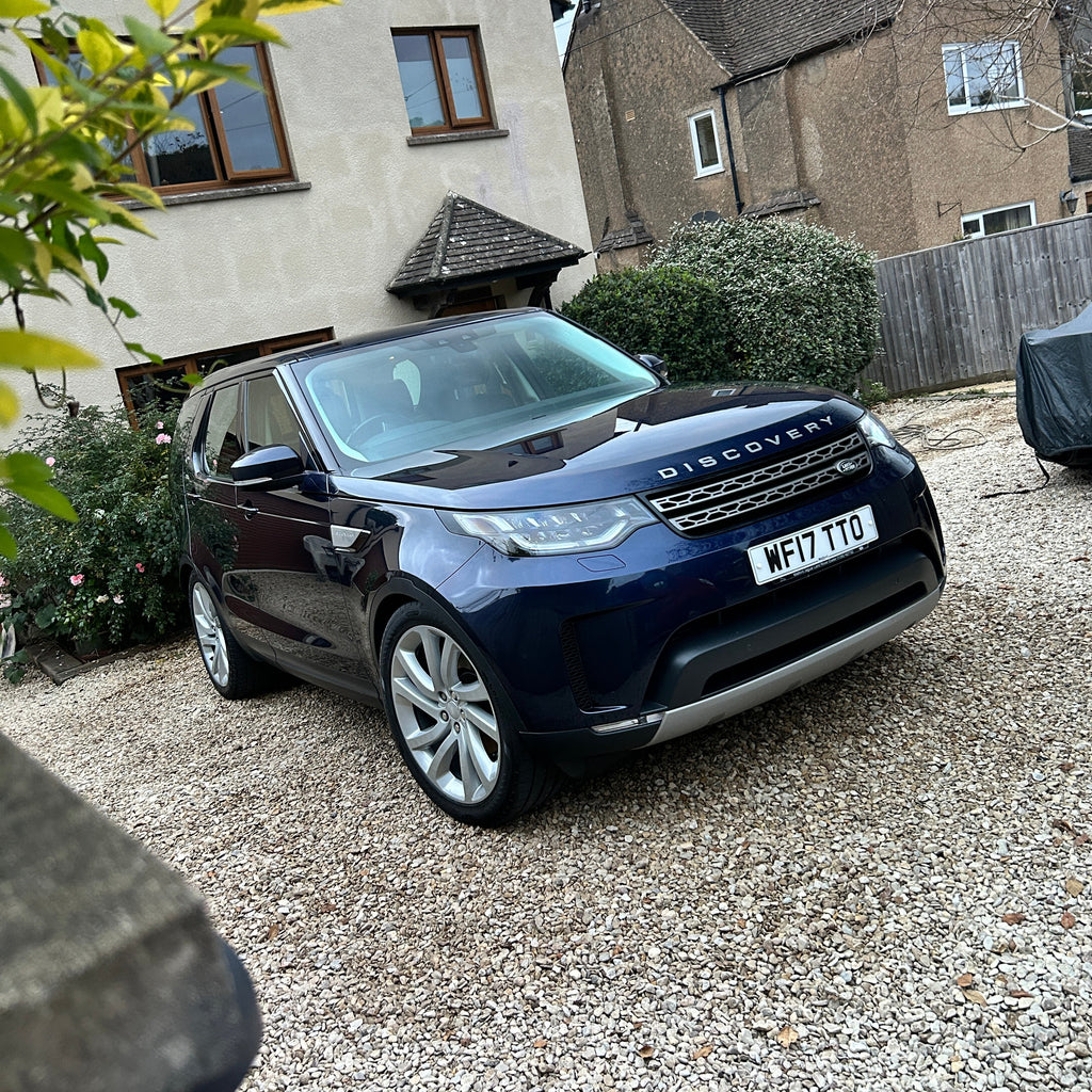 Black car parked on a driveway with houses in the background